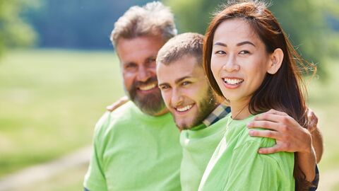 Drei Menschen mit einem hellgrünen T-Shirt lachen in die Kamera