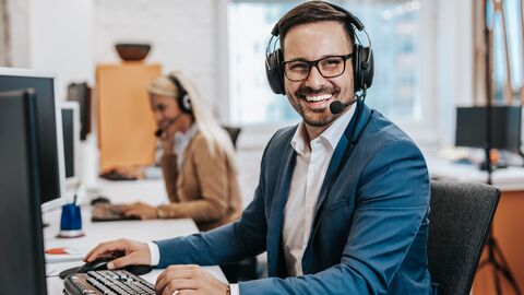 Mann mit Telefon-Kopfhörer lacht und hat die Hände an der Tastatur