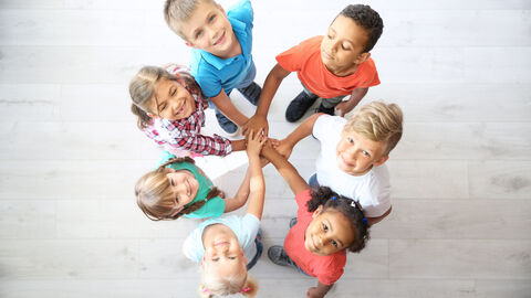 Mehrere Kinder stehen im Kreis und halten ihre Hände in der Mitte zwischen sich übereinander