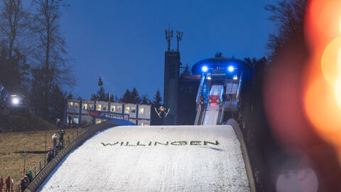 Skispringer springt von Schanze mit einem Schriftzug "Willingen" bei Nacht