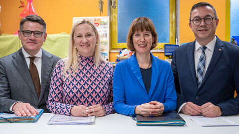 Zwei Frauen und zwei Männer stehen an Pult und lächeln in Kamera 