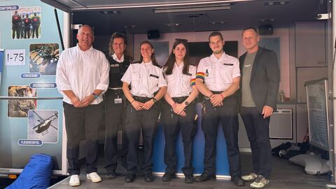 Vier uniformierte Personen stehen in einer Reihe im Polizeimobil, zwei von ihnen tragen Regenbogenarmbinden - links und rechts davon stehen Herr Poseck und Herr Müller.