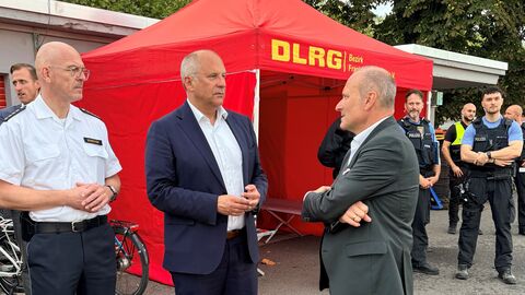 Herr Poseck und Herr Bosecker stehen nebeneinander zu Herrn Feda gewannt - im Hintergrund ein Pavillon der DLRG